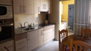 Cuina amb armaris de fusta clara, encimera de granit i zona de menjador amb taula i cadires.