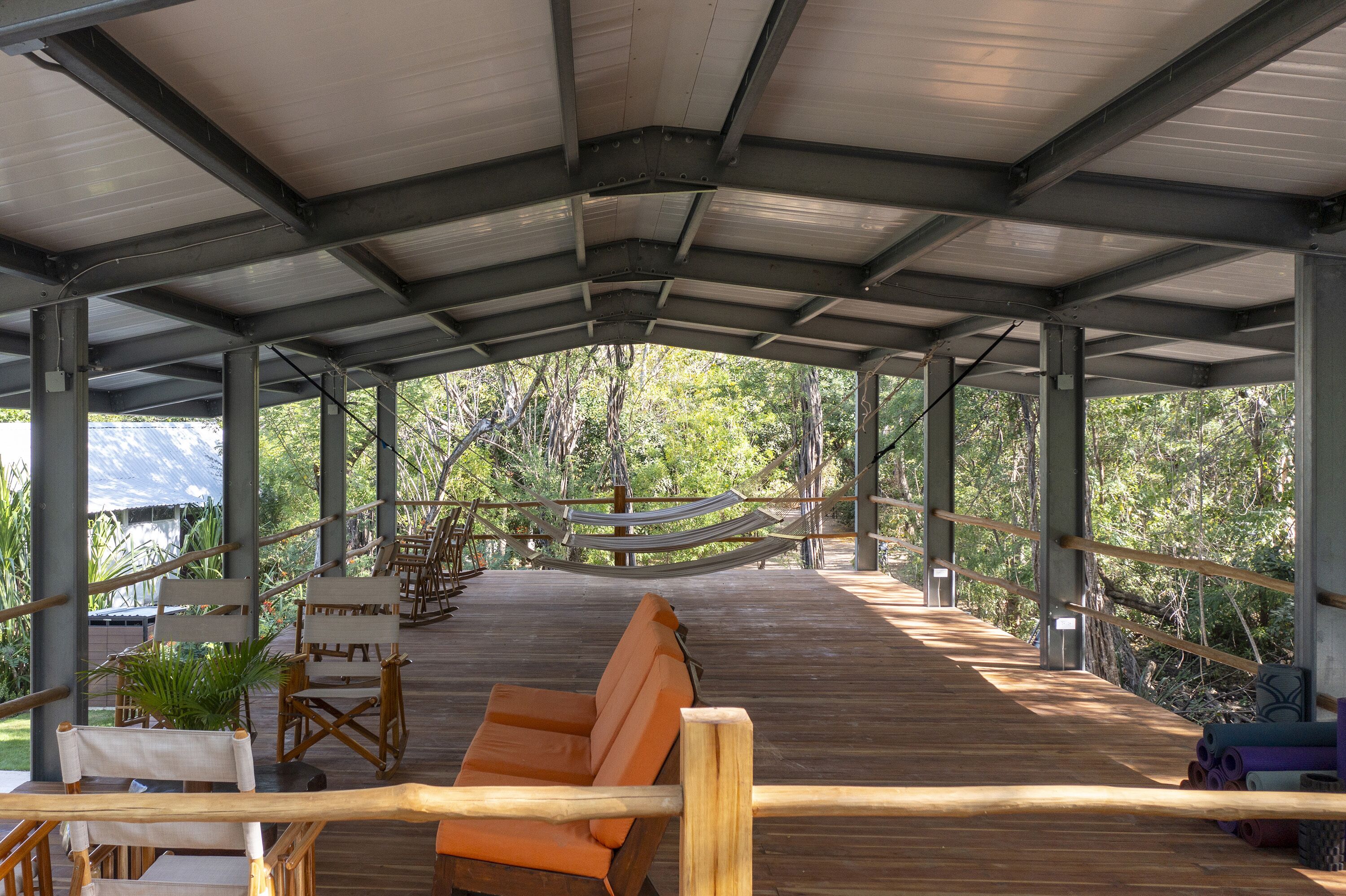 A covered wooden deck with seating, a hammock, and a view of the surrounding greenery.