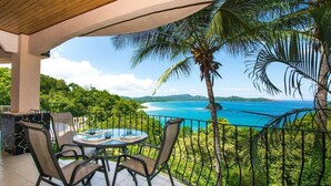 Ein Balkon mit Tisch und Stühlen mit Blick auf die Küste, Palmen und einen klaren Himmel.
