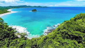Eine Küstenlandschaft mit Strand, klarem türkisblauem Wasser und üppigem Grün.