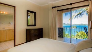 Ein Schlafzimmer mit Bett, Schminktisch, Spiegel und einem Balkon mit Meerblick.