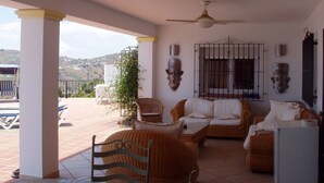 Un patio techado con muebles de mimbre, ventiladores de techo y vistas al paisaje.