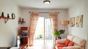 Una sala de estar con sofá, mesa de centro, televisor y una ventana con cortinas.