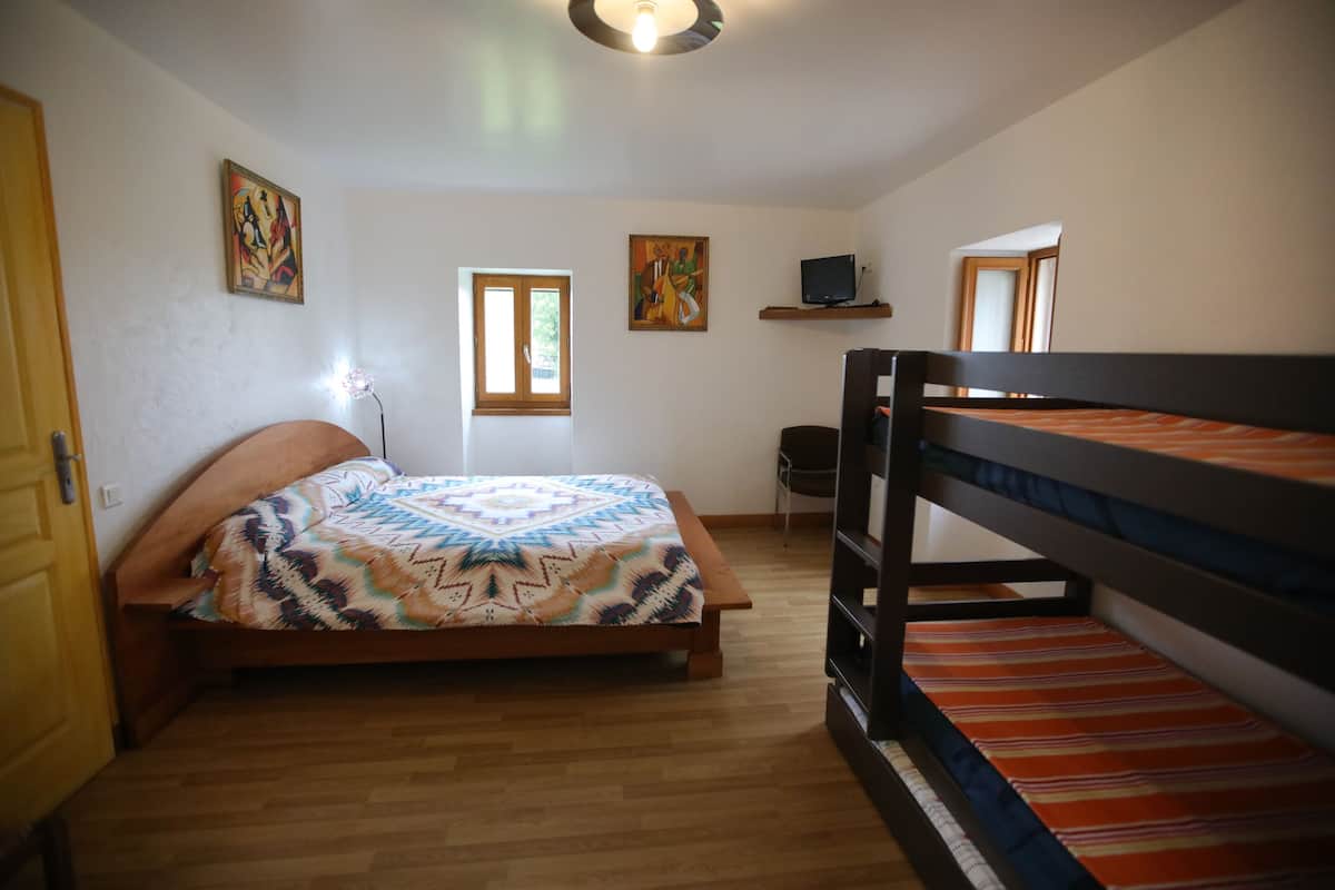 A bedroom with a bed, bunk beds, a desk, and two windows.