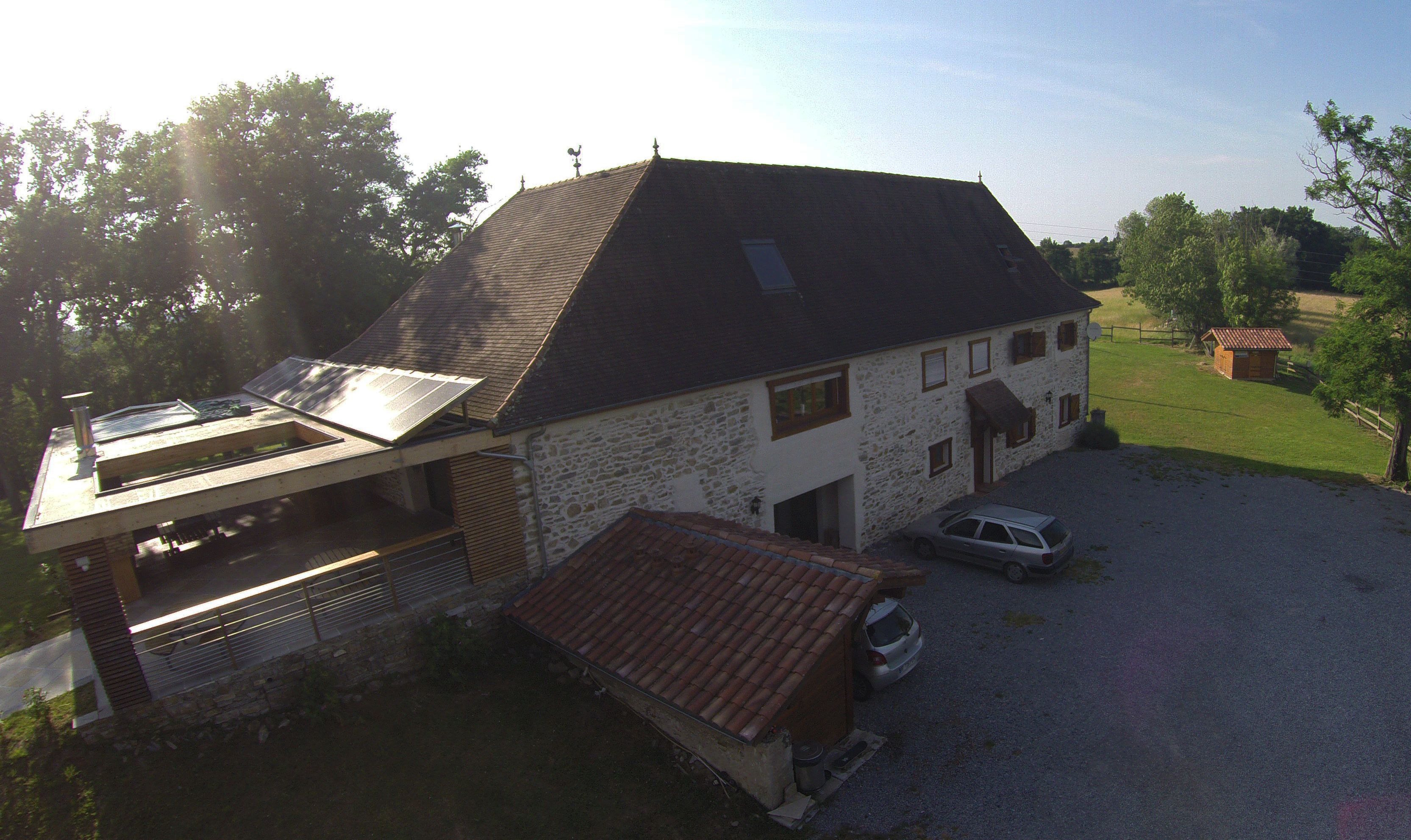 A two-story stone house with a sloped roof, a carport, and a small shed.