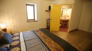 A bedroom with a bed, a window, a door leading to a bathroom, and a bedside table with a lamp.