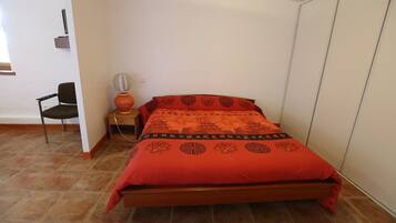 Un dormitorio con cama, una silla, una mesita de noche y un estante en la pared.