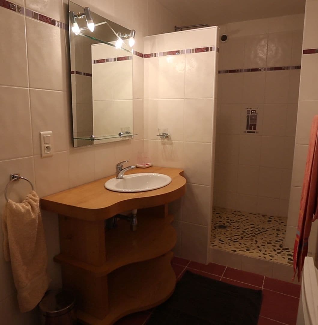 Ein Badezimmer mit einem Holzkosmetikschrank, einem Spiegel und einem Duschbereich.