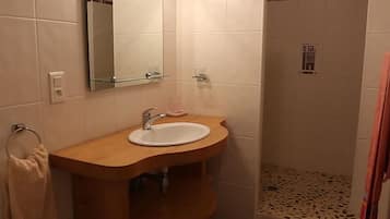Ein Badezimmer mit einem Holzkosmetikschrank, einem Spiegel und einem Duschbereich.