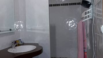 Un baño con lavamanos, espejo, ducha y toallero.