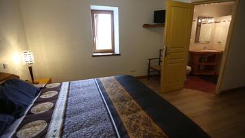 A bedroom with a bed, a nightstand, a lamp, a window, and an open door leading to a bathroom.