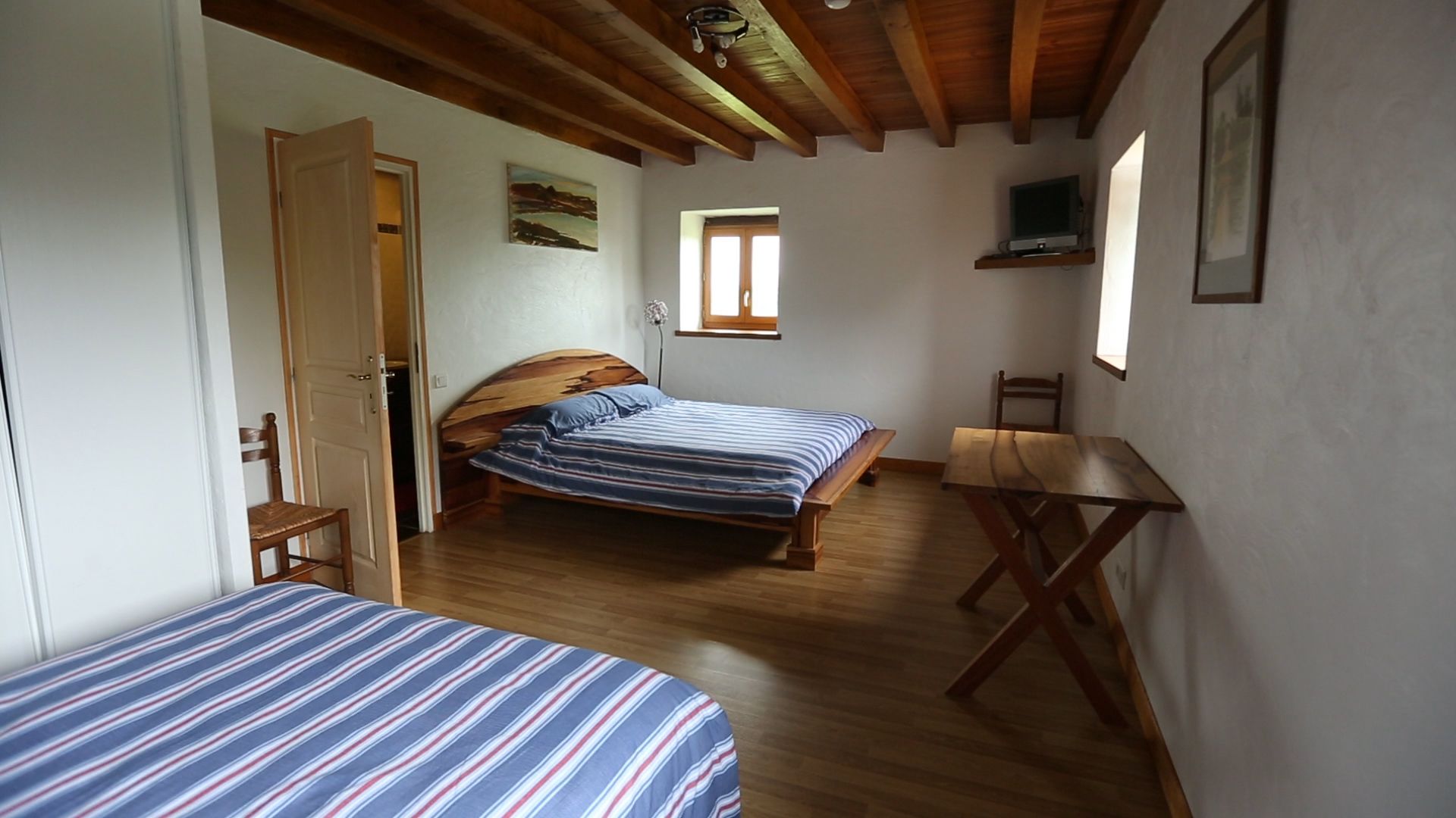 A bedroom with two beds, a wooden desk, and a small window.