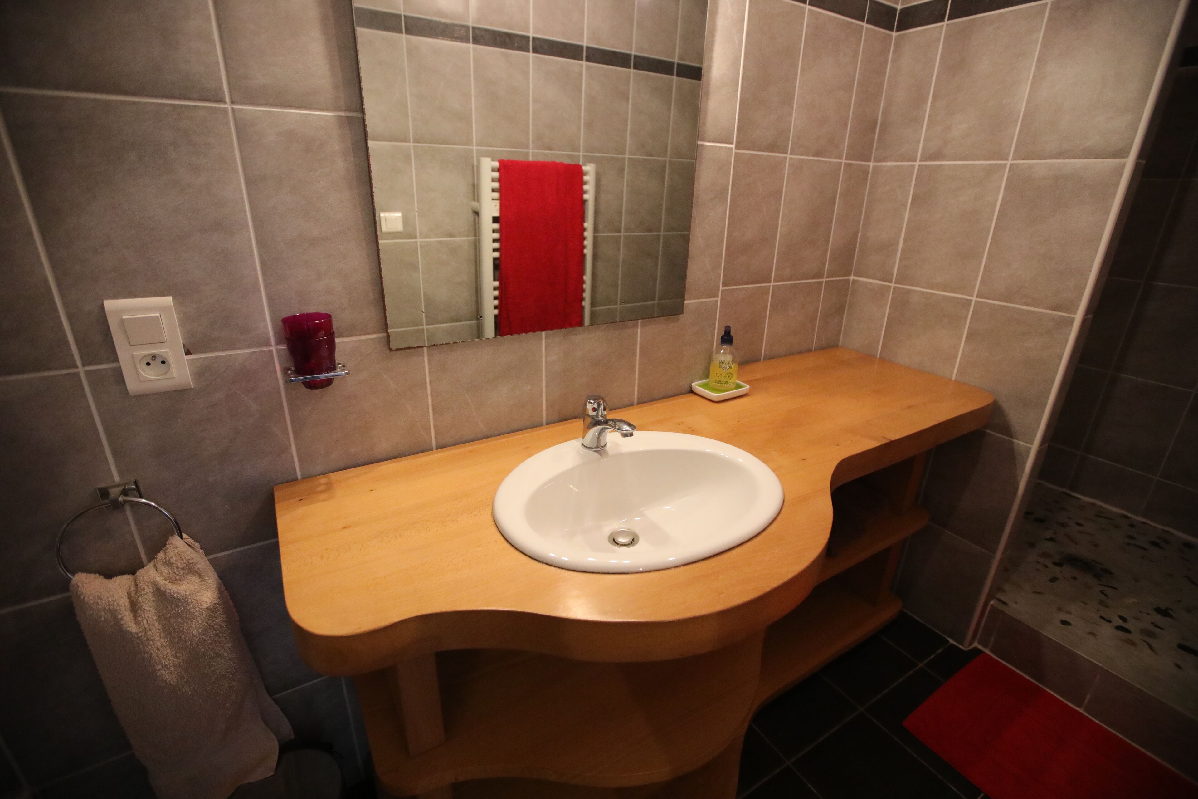 A bathroom with a wooden vanity, a white sink, a red towel, and a mirror.