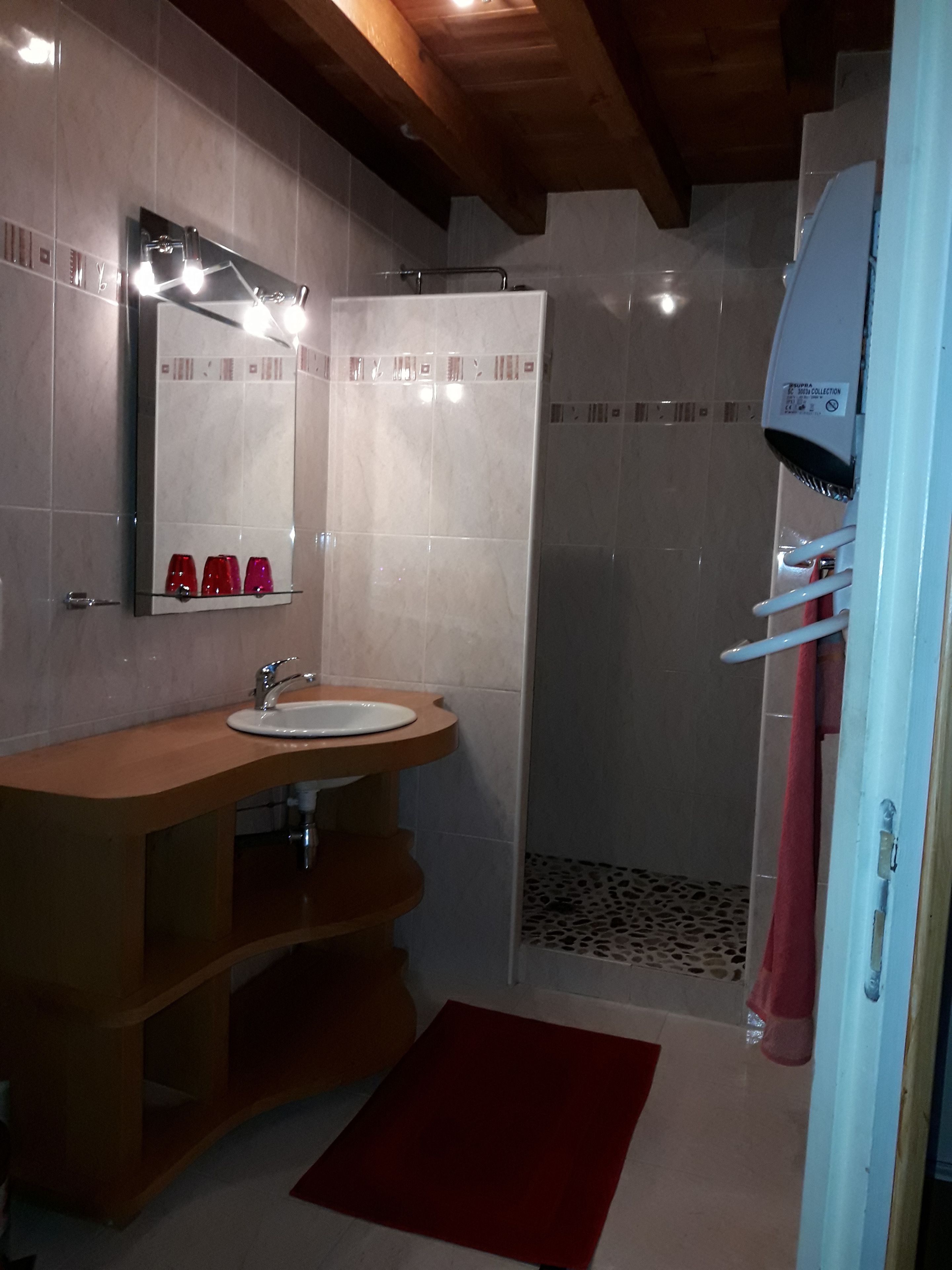 A bathroom with a wooden vanity, a sink, a mirror, and a shower area.