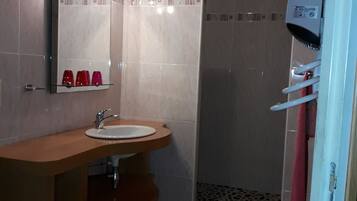 A bathroom with a wooden vanity, a sink, a mirror, and a shower area.