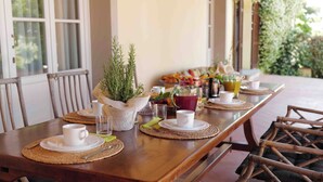 A dining table set with white cups, plates, and cutlery, surrounded by wicker chairs.