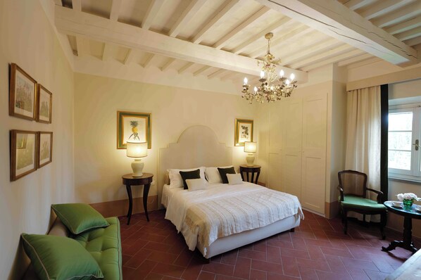 A bedroom with a large bed, two bedside tables with lamps, a chair, a small table with a vase, and a window with curtains.