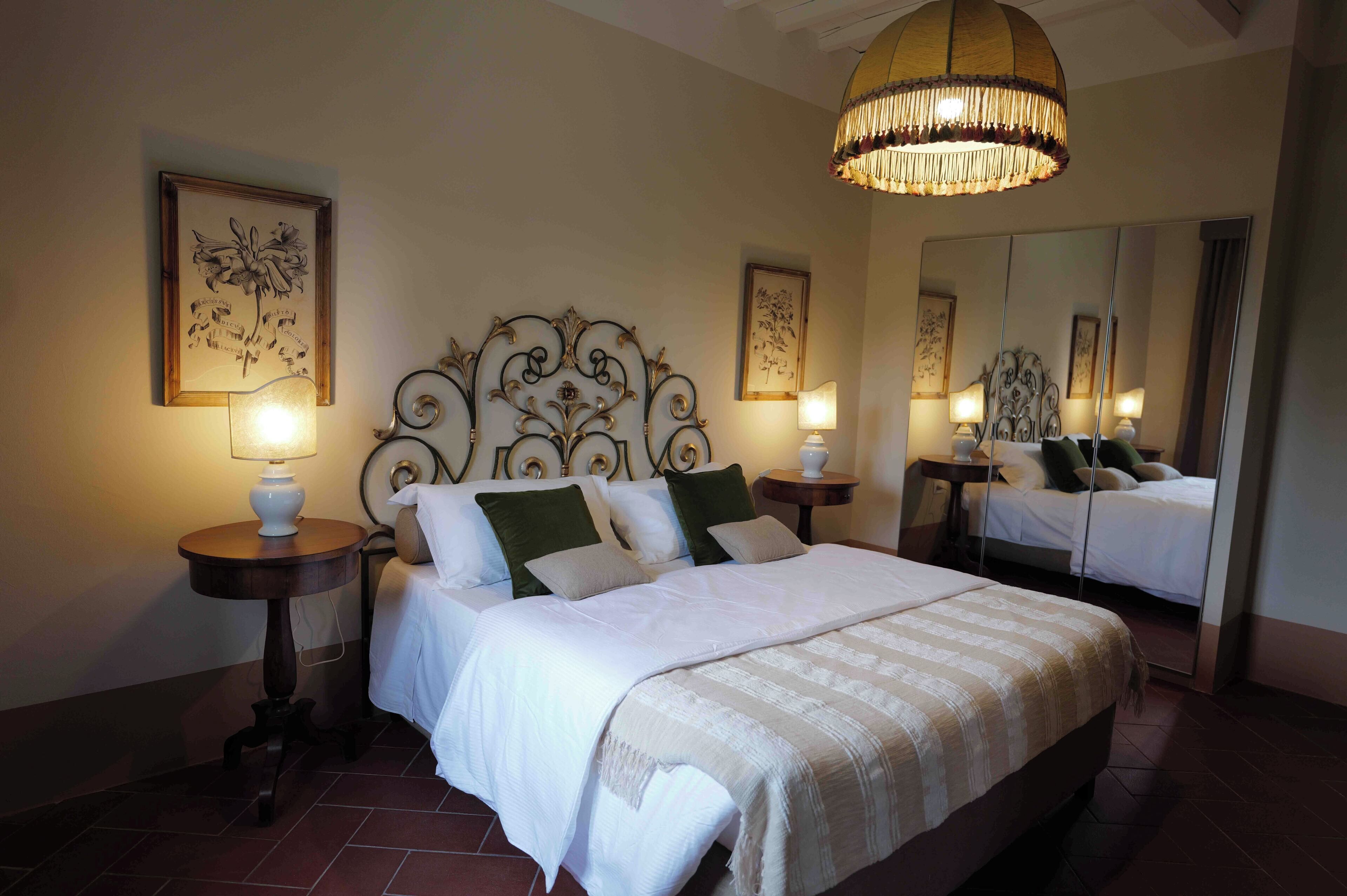 Un letto rifatto con lenzuola bianche e una testiera decorativa, due comodini con lampade e opere d'arte incorniciate alle pareti.