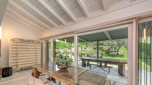 Un comedor moderno con una mesa y sillas de vidrio, un banco de madera afuera y vistas a un jardín a través de amplios puertas correderas.