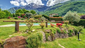 Un jardín con cerca de madera, piscina y montañas al fondo.