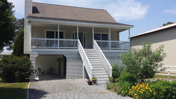 A two-story house with a covered porch, a staircase, and a small outdoor seating area. - Close to Beach! 2026 Prime Weeks Available!  Family Oriented Home! Dogs Welcome! (Bethany Beach)