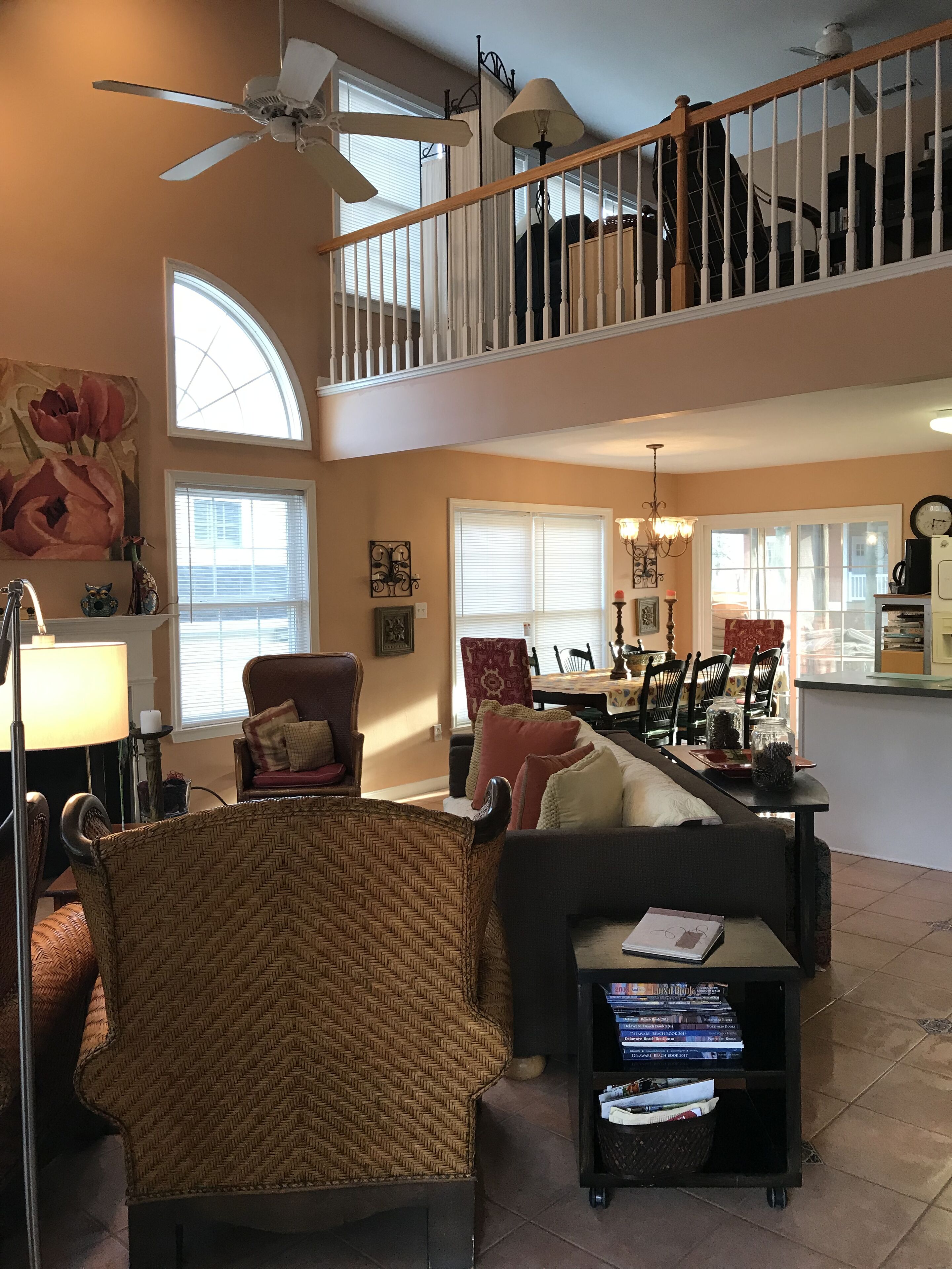 A spacious living room with a high ceiling, a dining area, and a staircase leading to an upper level.