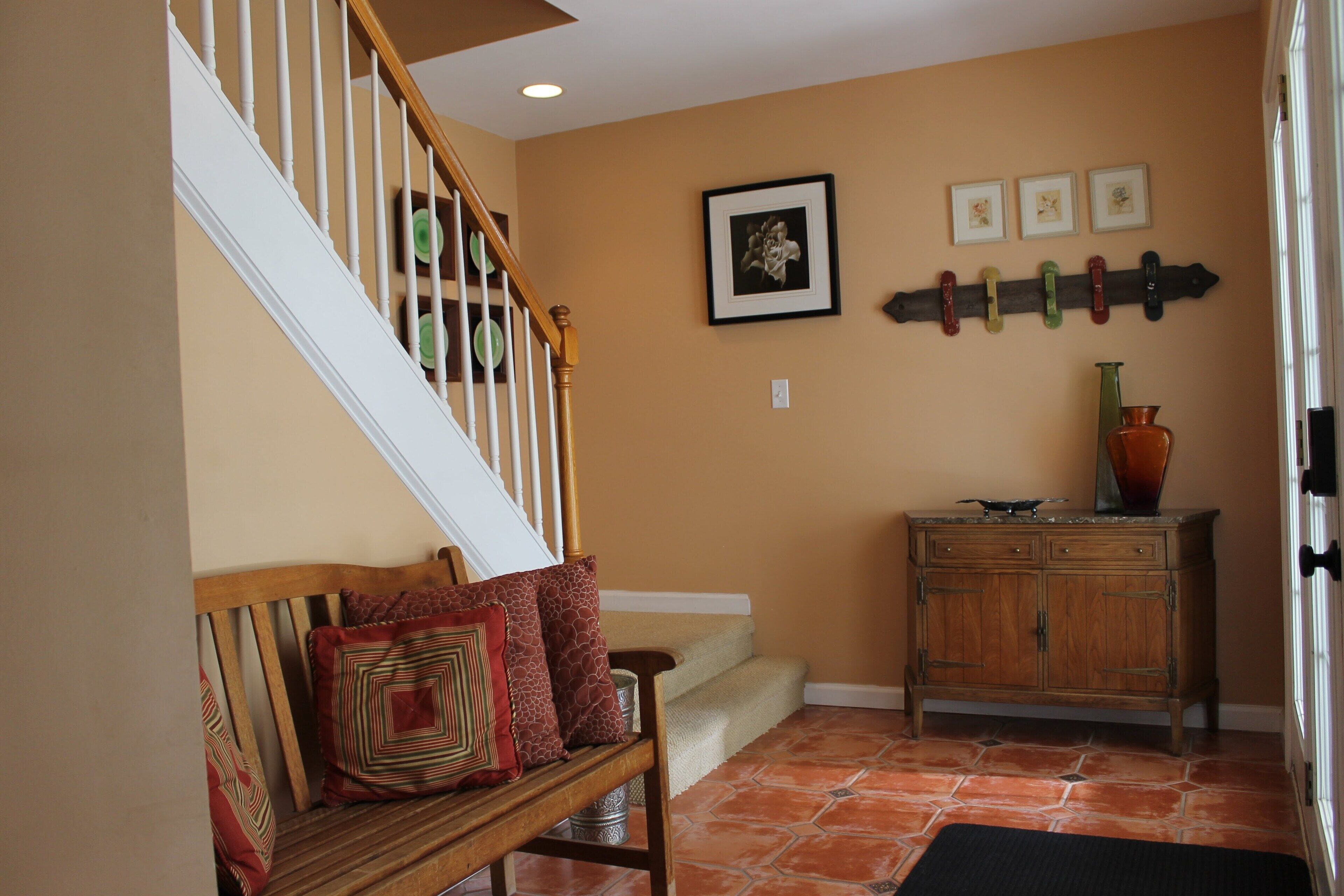 A staircase with a wooden handrail, a bench with patterned cushions, a wall-mounted coat rack, and a cabinet with decorative items.