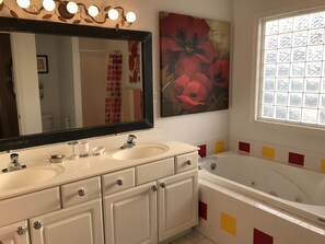 A bathroom with two sinks, a large mirror, a bathtub, and a window with frosted glass.