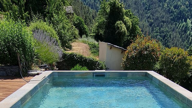 A rectangular swimming pool with clear blue water, surrounded by a wooden deck and a stone border. In the background, there is a lush green mountain and a small white building. - Castineta: mansion - CastinetaHouse with character (Castineta)