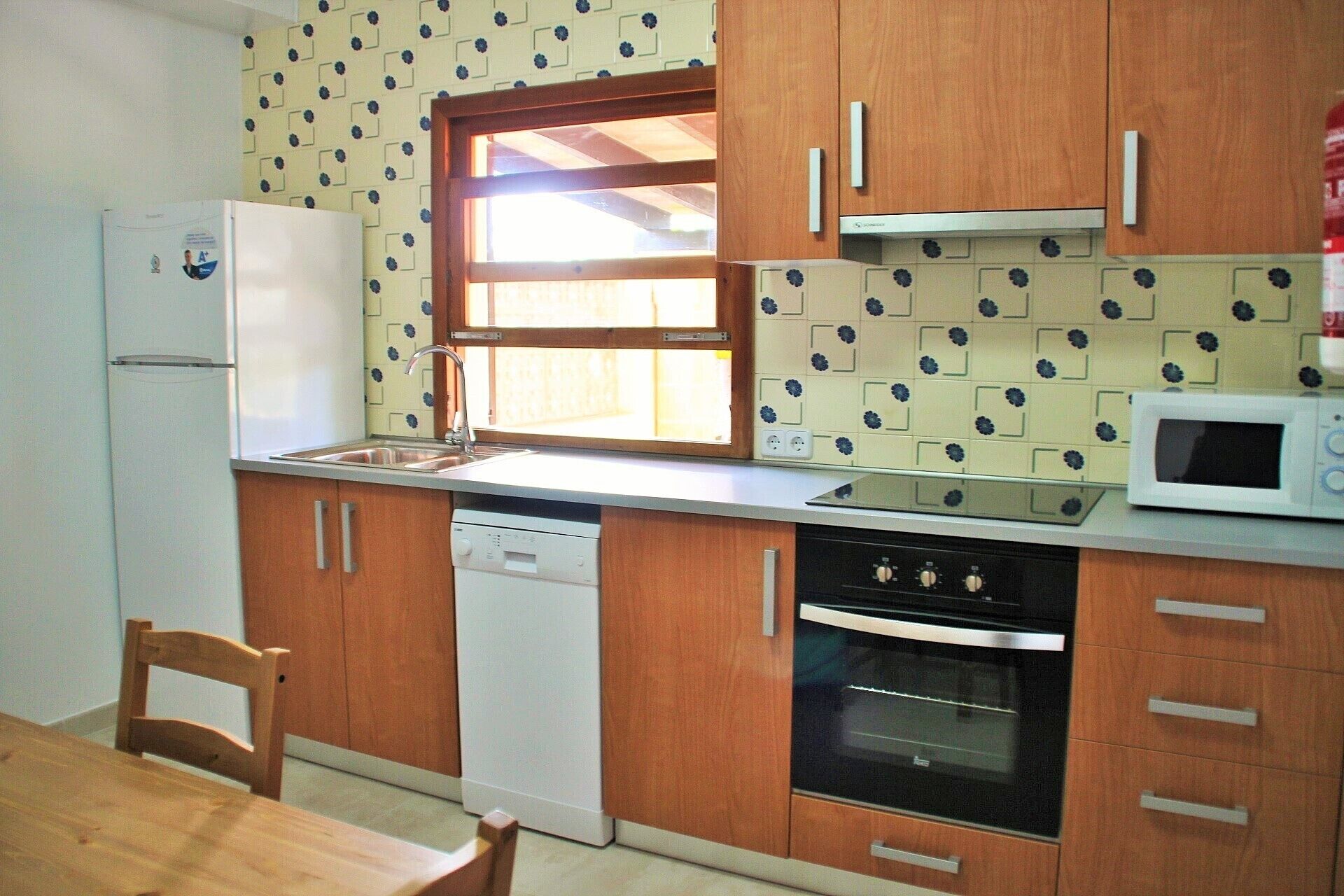 A kitchen with wooden cabinets, a white refrigerator, a microwave, a dishwasher, and a window above the sink.