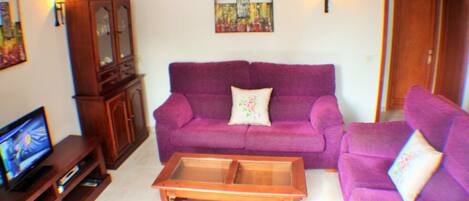A living room with a purple sofa, a wooden coffee table, and a television on a wooden stand.