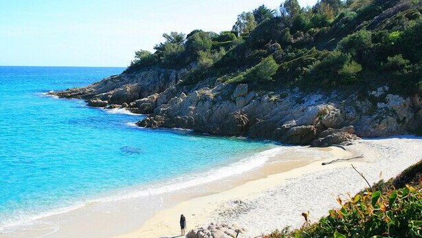 Una spiaggia con acque turchesi cristalline, una costa sabbiosa, scogliere rocciose e vegetazione.