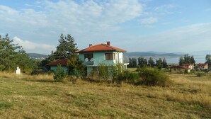 A two-story house with a red-tiled roof, surrounded by a grassy field and trees. - Spacious, Well-Equipped Villa With Stunning Views & Multiple Leisure Opportuni (Batak)