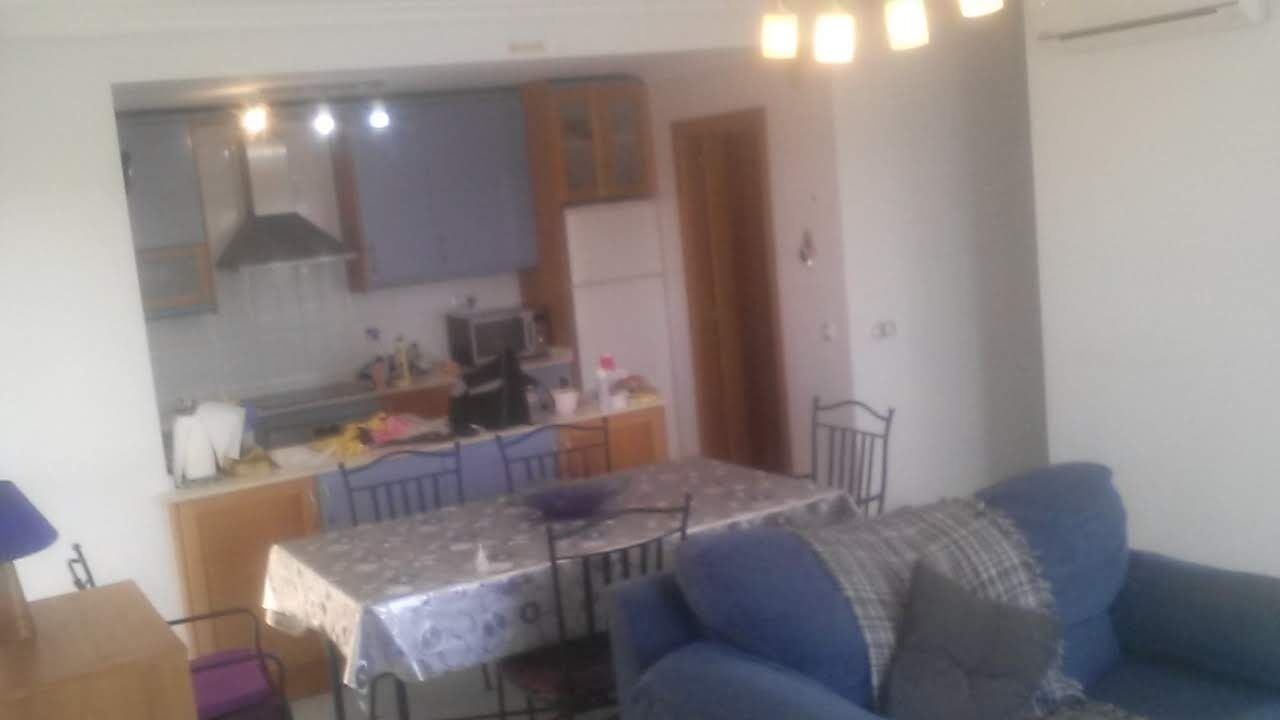 Un espai vital reduït amb zona cuina, taula de dinar i sofà blau.