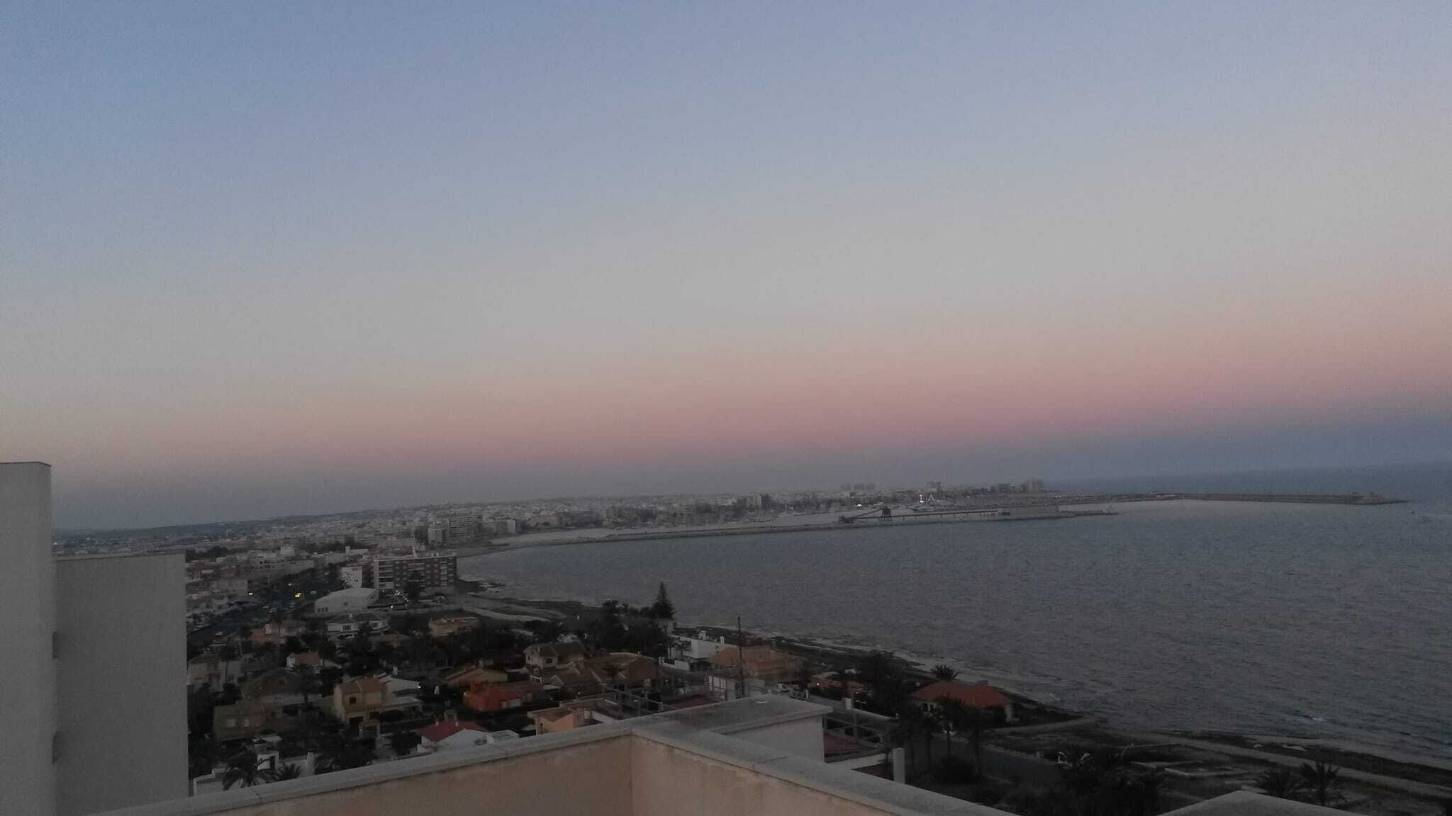 Un paisaje urbano costero al atardecer con edificios a lo largo del frente marítimo y una vista despejada del mar.