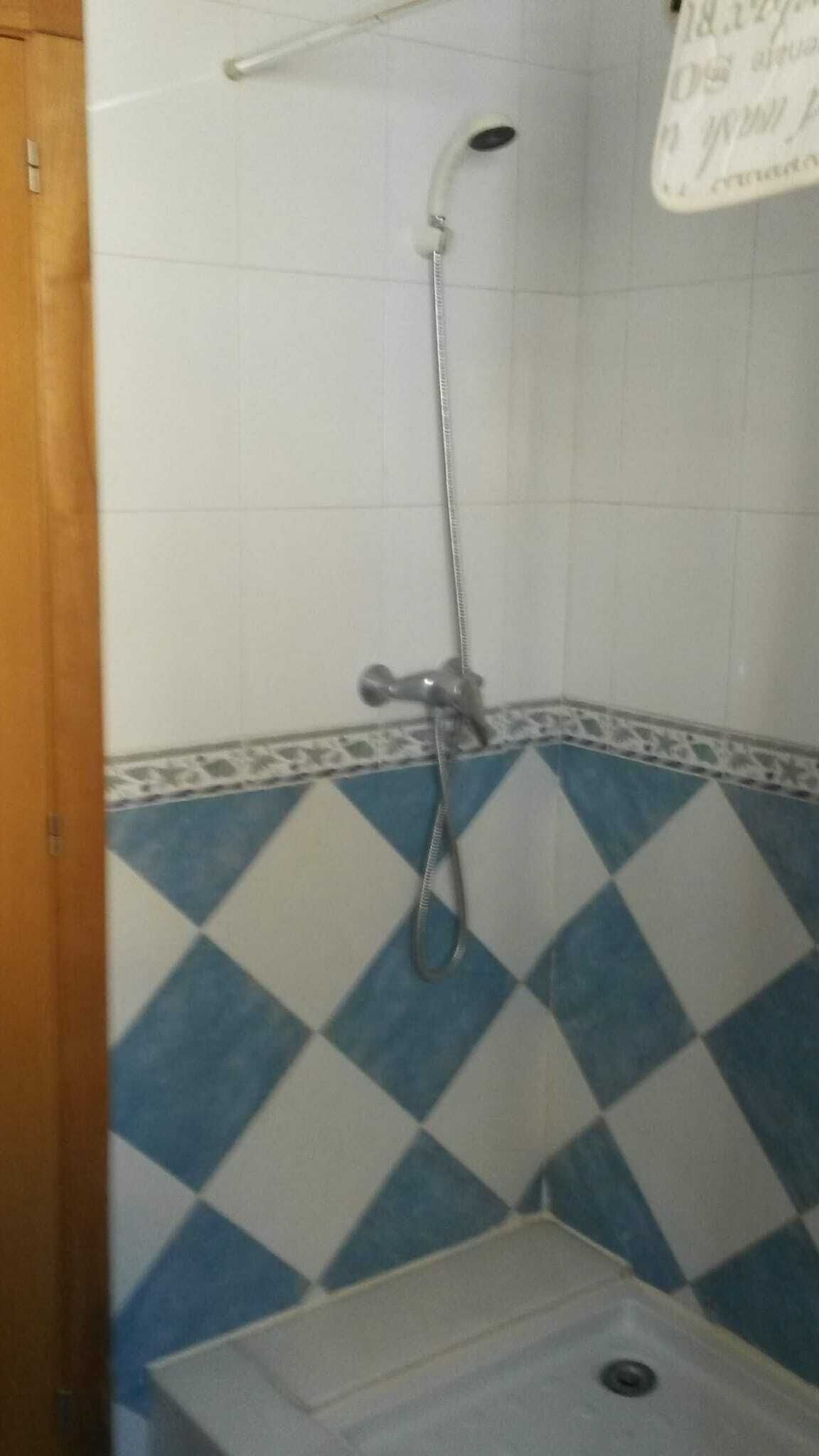 Un baño con ducha, lavabo y piso de baldosas con diseño azul y blanco.