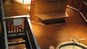 Een houten terras met een jacuzzi, een klein zitgedeelte en een trap naar een hoger gelegen niveau.