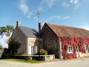 A stone building with a sloped roof and a chimney, adjacent to a smaller structure with red ivy.