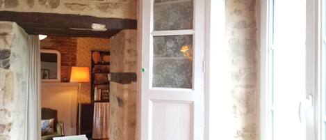 A rustic room with exposed stone walls, a wooden door, a small table with a green cloth, and a red patterned rug.
