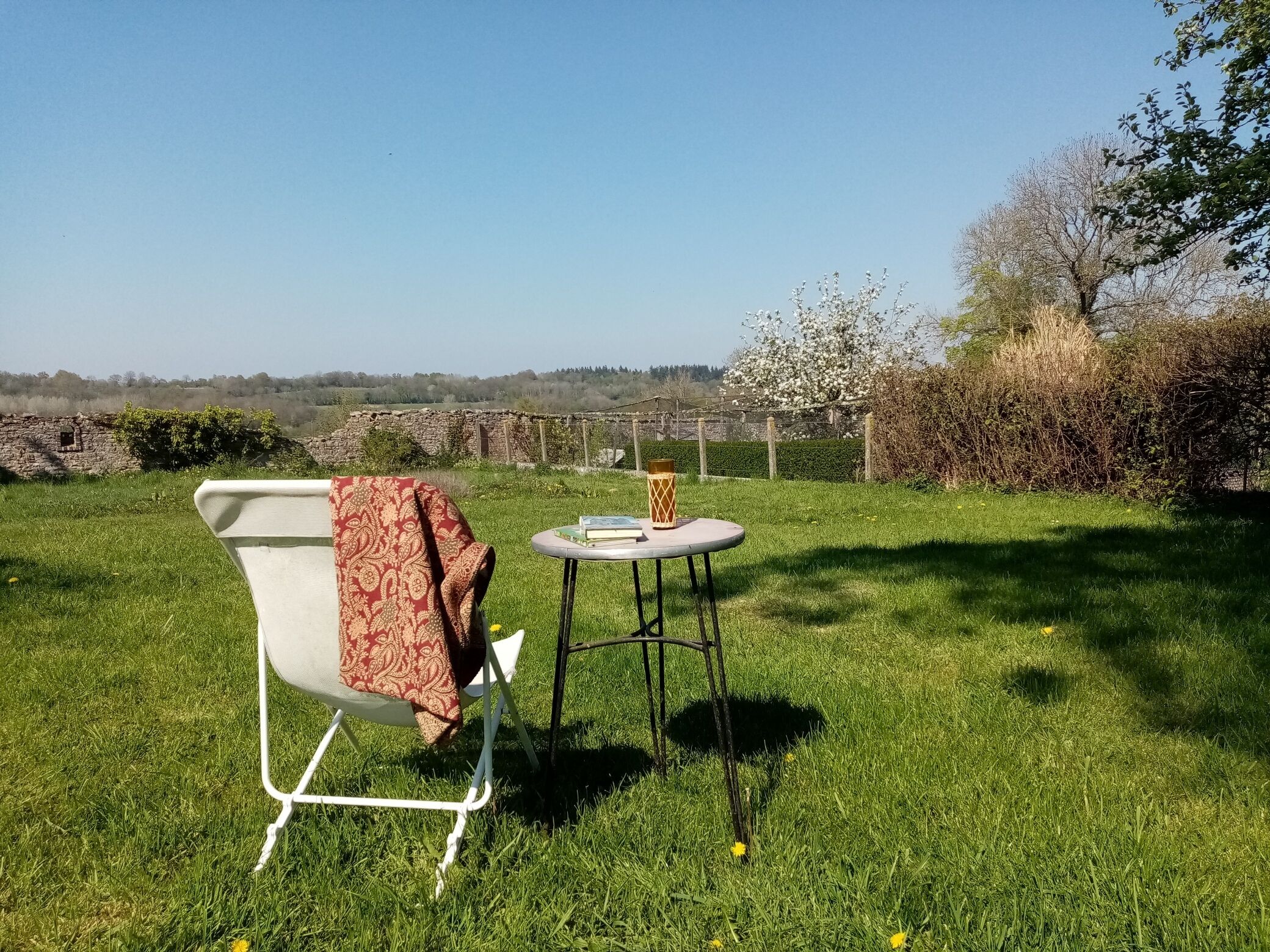 A grassy outdoor area with a white chair and a small round table with a book and a decorative vase.