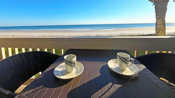 A table with two white cups and saucers, overlooking a beach. - Crescent Beach I-14 Four Winds Condo (St Augustine)