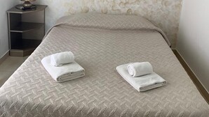 A neatly made bed with two folded towels, a small bedside table with a lamp, and a textured wall.