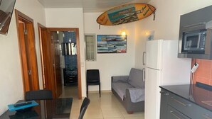 A compact living space with a dining table, chairs, a sofa, a kitchen area with a microwave, and a surfboard decoration.