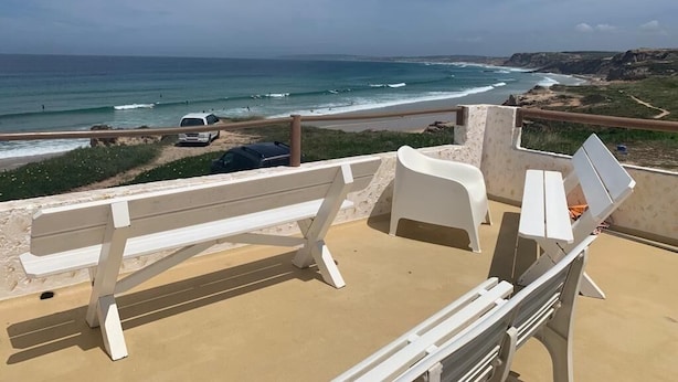 A beachside terrace with a white bench and lounge chairs, overlooking the ocean.