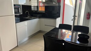 A compact kitchen with white cabinets, a black countertop, a microwave, a sink, and a dining table with chairs.
