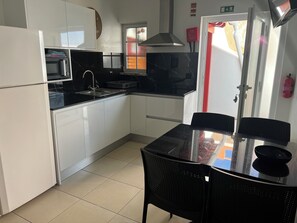 Une cuisine compacte avec des meubles blancs, un plan de travail noir, un four à micro-ondes, un évier et une table à manger avec des chaises.