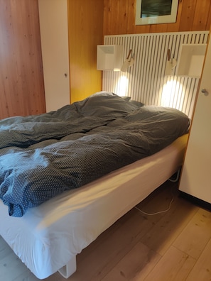 Un lit simple avec un matelas blanc, une couverture à pois foncés et un plancher en bois.