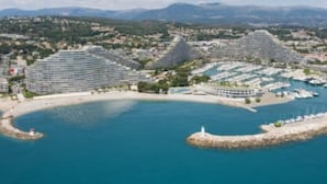 Un complejo turístico frente al mar con varios edificios de hotel, un puerto deportivo y una costa curva.