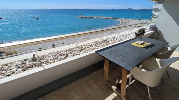 Un balcón con vista al mar, una mesa y sillas.