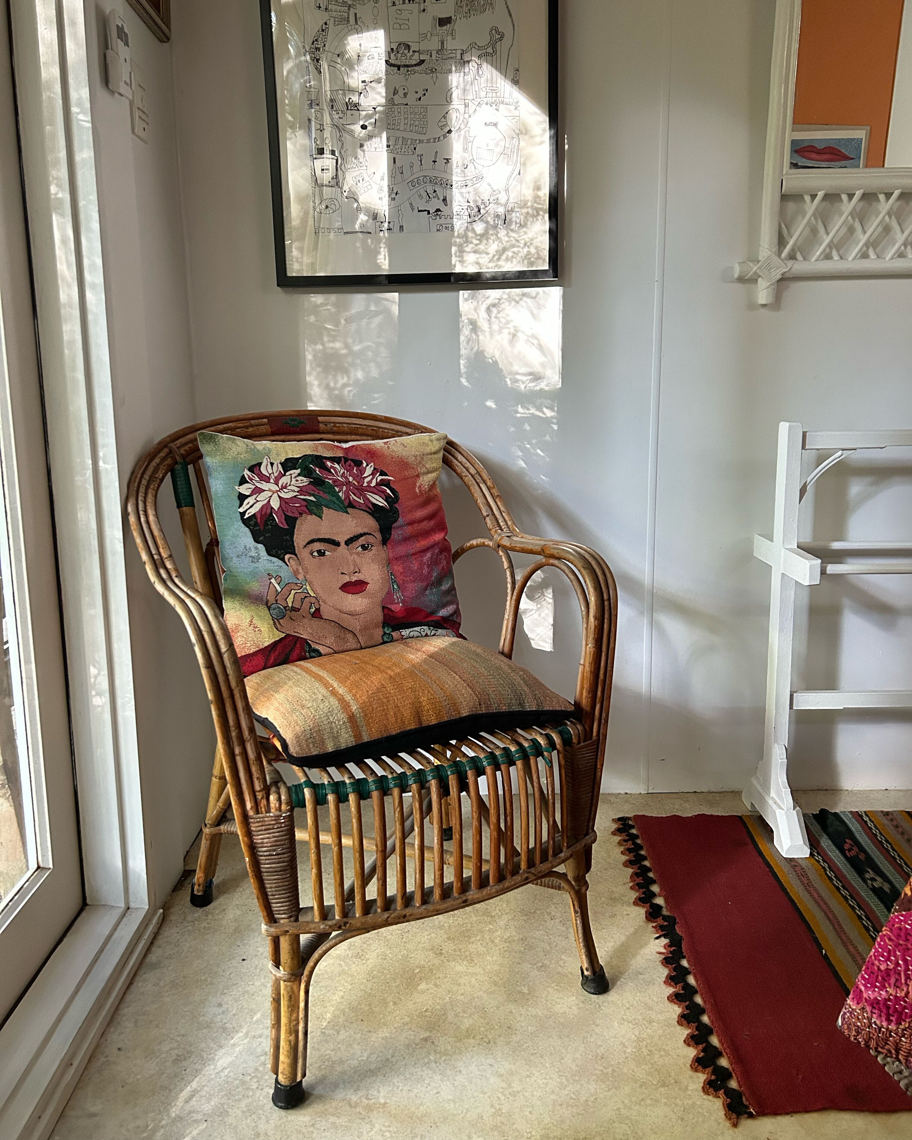 Une chaise en osier avec un coussin, un tapis rouge et une carte encadrée accrochée au mur.